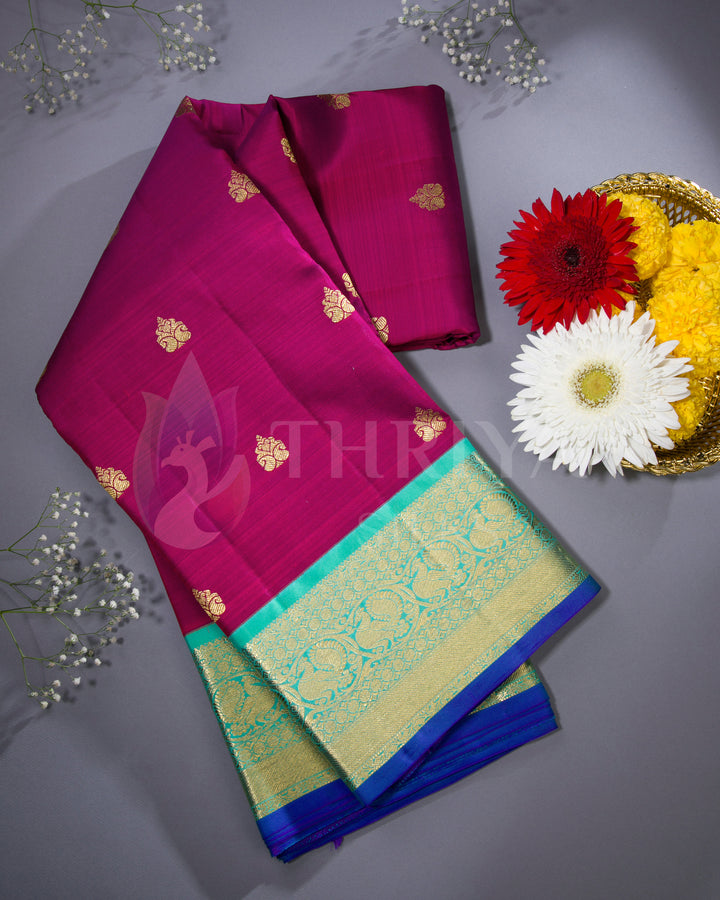 Styled image of magenta silk saree with green and gold border alongside floral decor