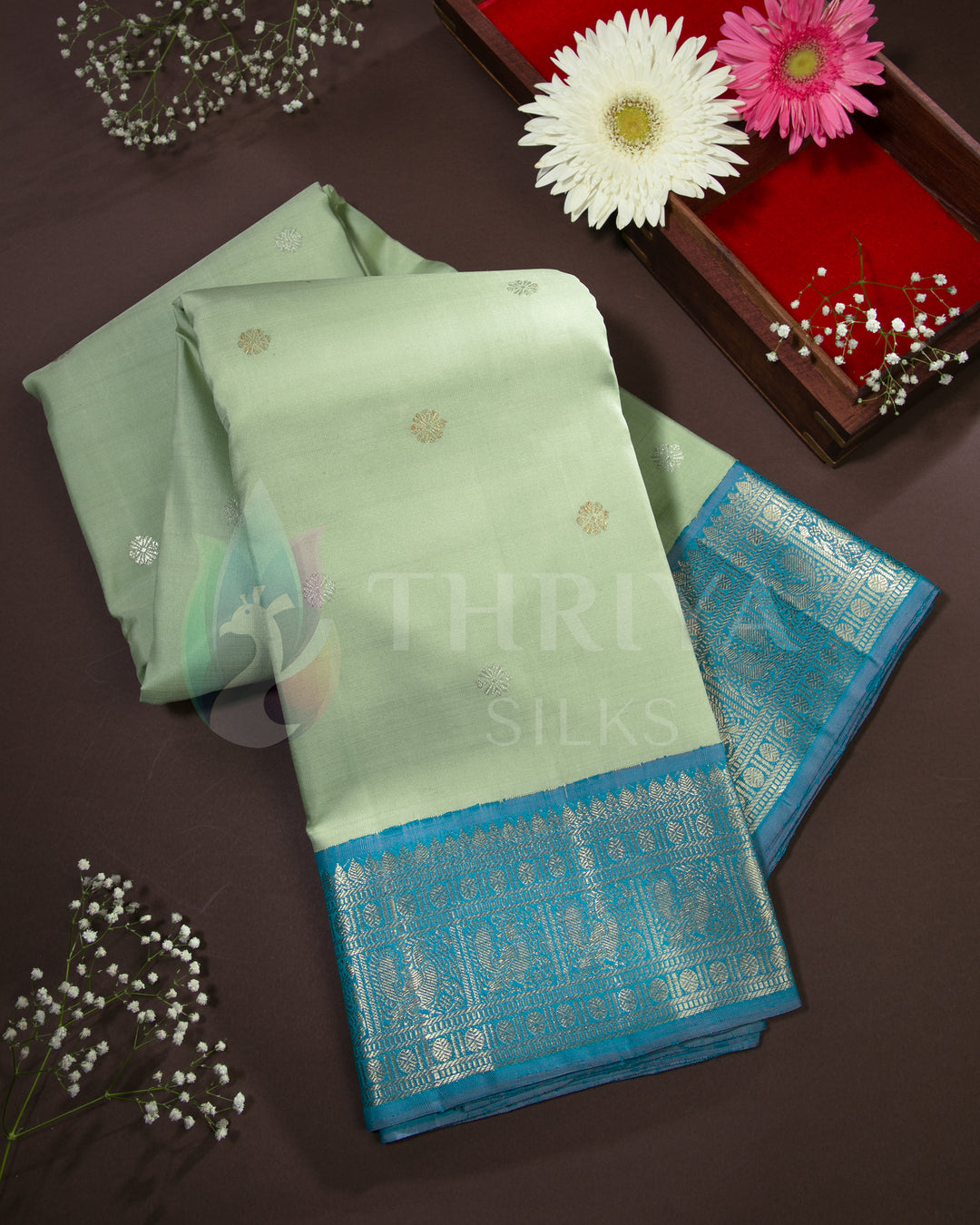 Styled image of pastel green silk saree with turquoise blue zari border and floral decor