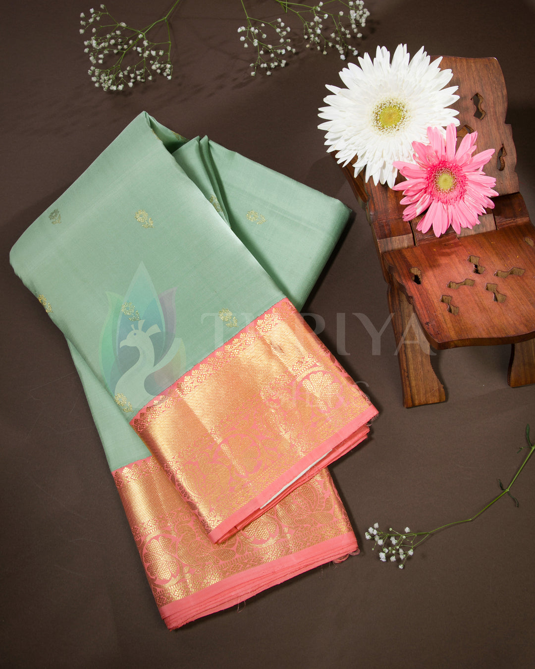 Styled presentation of pastel green silk saree with gold zari border and peach-pink pallu