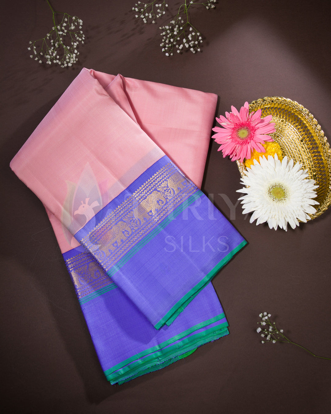 Folded peach pink and violet Kanjivaram silk saree styled with flowers and a decorative golden tray