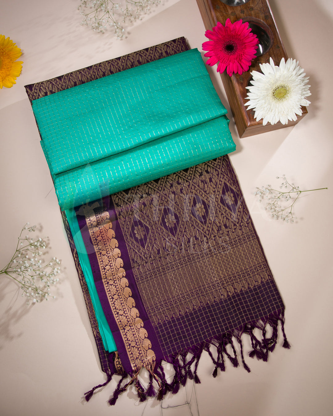  Folded view of teal green and purple silk saree with gold zari pallu and tassel detailing