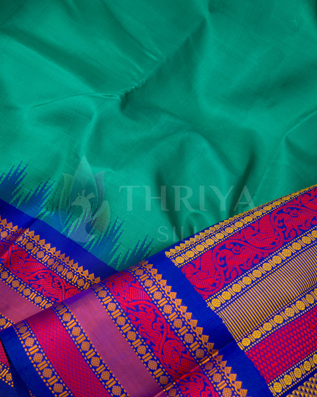 Close-up of teal silk saree fabric and intricate magenta zari border – traditional craftsmanship by Thriya Silks
