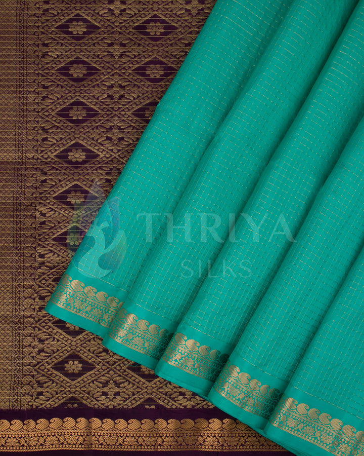 Detailed view of pleats and pallu featuring teal green body and diamond-shaped zari motifs on the purple base.