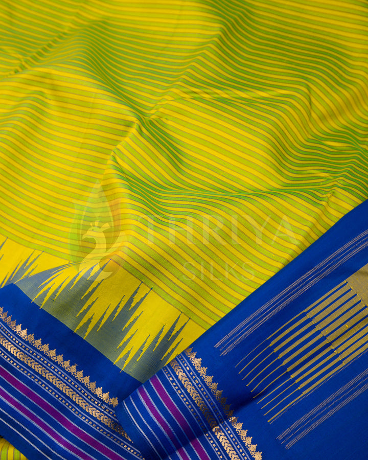 Close-up of yellow-green silk saree fabric showing detailed blue and gold border work, Thriya Silks